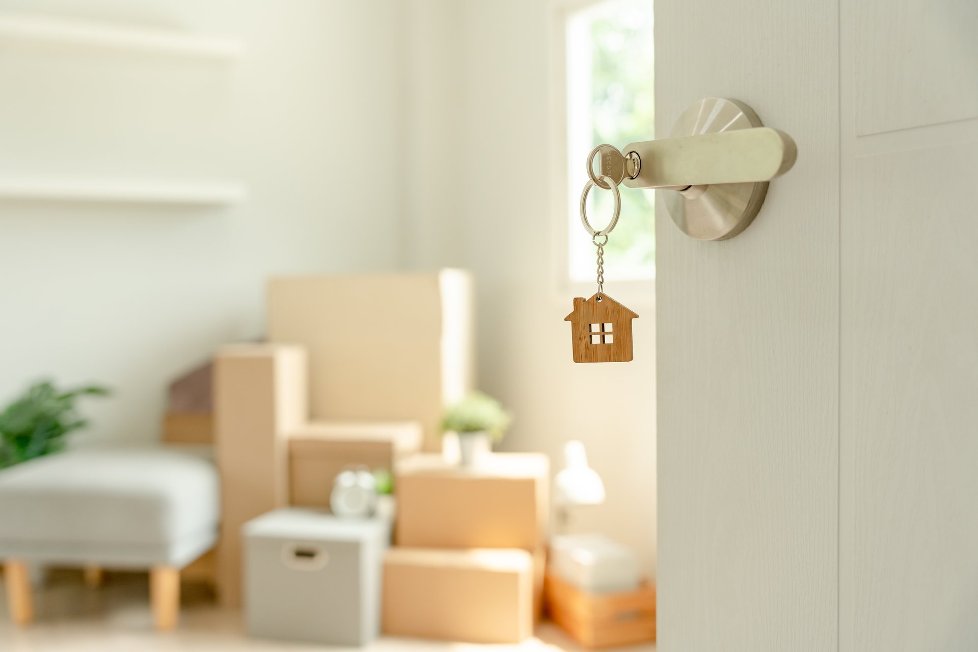 Moving house, relocation. The key was inserted into the door of the new house, inside the room was a cardboard box containing personal belongings and furniture.
