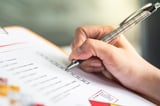 Action of a safety supervisor hand is checking on checklist of chemical and hazardous material form to verify the risk with blurred background of factory storage workplace.