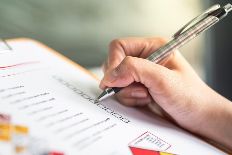 Action of a safety supervisor hand is checking on checklist of chemical and hazardous material form to verify the risk with blurred background of factory storage workplace.