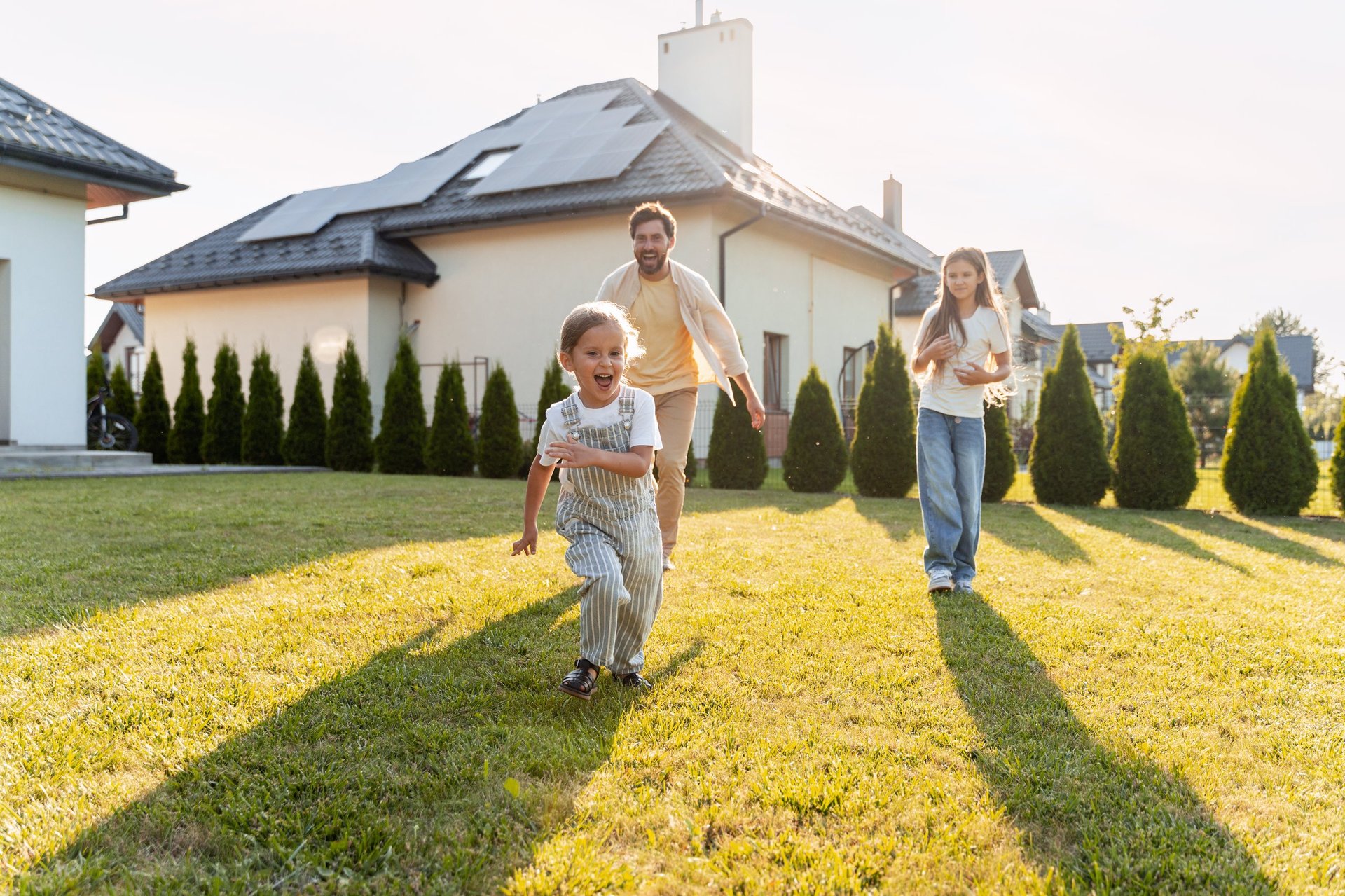 Father and children running on the lawn in front of their house, enjoying a sunny day