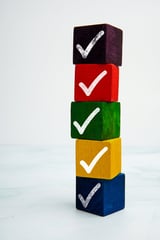 Stacked colorful cubes with white check marks, representing task completion and approval concept on light background.