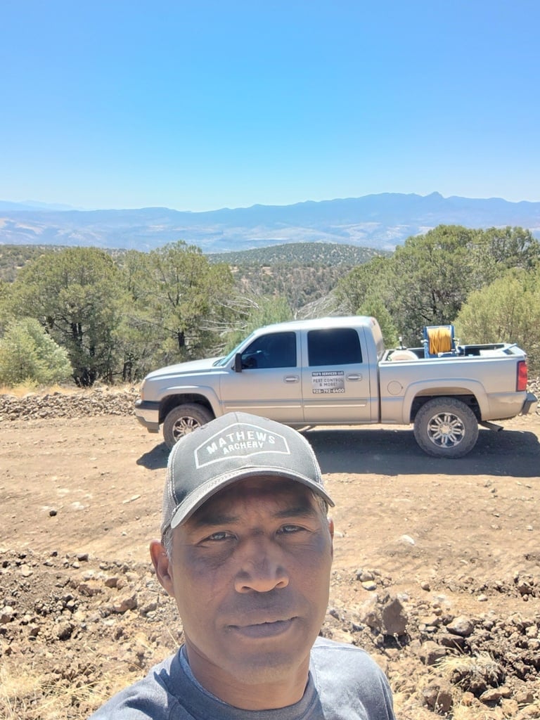 Man in baseball cap takes selfie with pickup truck and mountain landscape in background